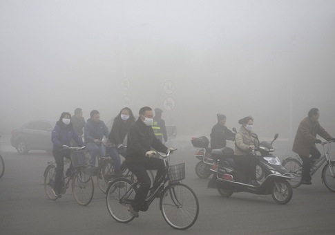 People ride along a street on a smoggy day in Daqing