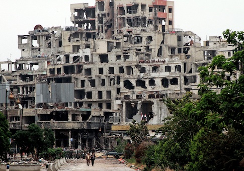 Syrian government officials walk on a road, back dropped, by damaged buildings from fighting with Free Syrian Army fighters in the old city of Homs, Syria