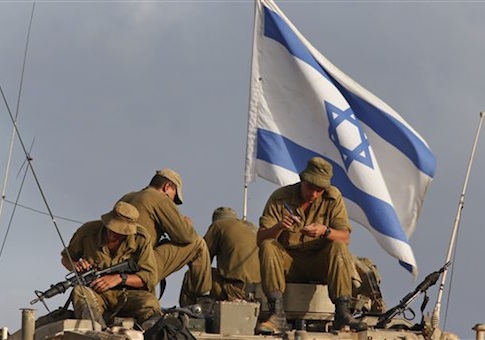 Israeli soldiers, backdropped by the national flag, sit on their armored personnel carrier as they clean their weapons