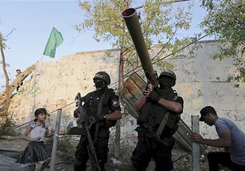 A Palestinian girl looks at masked militants of Izzedine al-Qassam Brigades, military wing of Hamas, celebrate at a victory rally at the debris of destroyed houses in Shijaiyah, neighborhood of Gaza City, in the northern Gaza Strip, Wednesday