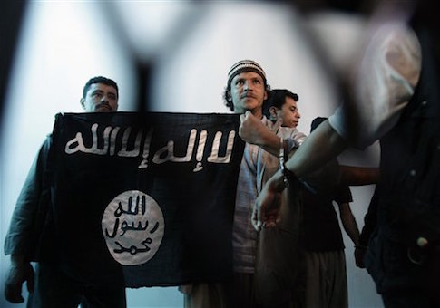 A suspected Yemeni al-Qaeda militant, center, holds a banner as he stands behind bars during a court hearing in state security court / AP