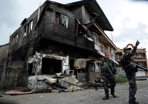 Local police inspect buildings burned down during aerial bombings in the city besieged by armed ISIS-linked militants