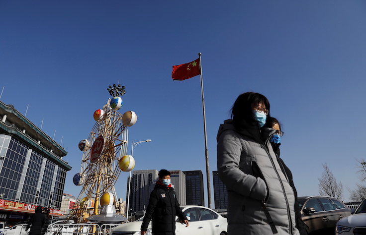 People wearing face masks walk past a Chinese flag, following new cases of the coronavirus disease (COVID-19) in the country, in Beijing